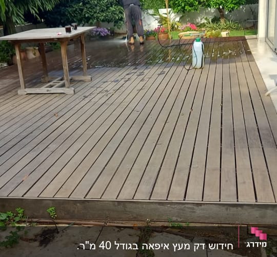 דק עץ עם שולחן, כיסאות ואדם מנקה עם צינור מים